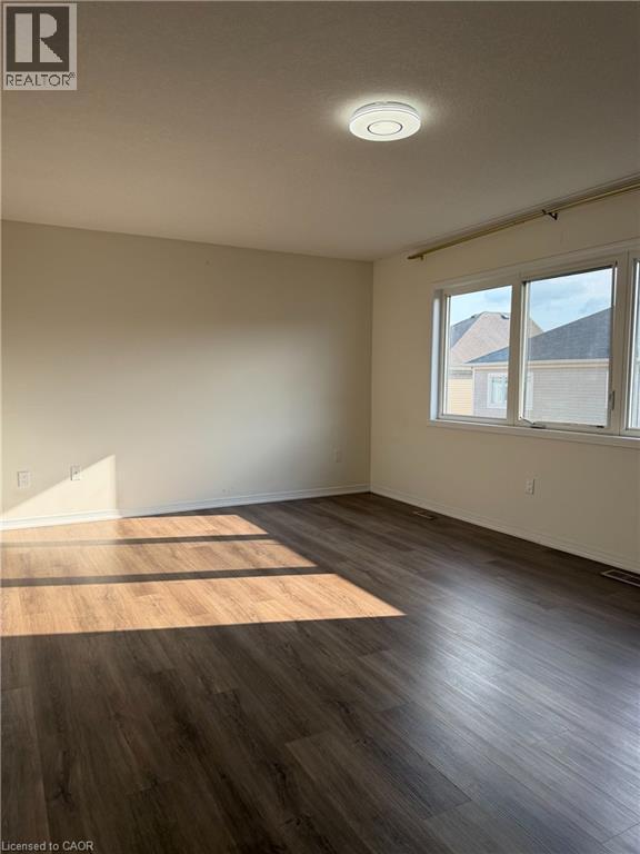 Spacious room featuring wood-finish flooring, neutral-toned walls, and a large window with white trim - 235 Apple Hill Crescent, Kitchener, ON