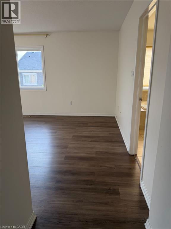 Spacious room featuring dark wood-finish flooring, white baseboards, and neutral wall paint - 235 Apple Hill Crescent, Kitchener, ON