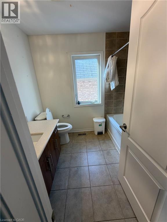 Bathroom featuring a single window, tiled flooring, wood-finish vanity with countertop, and a shower-tub combination with tiled surround - 235 Apple Hill Crescent, Kitchener, ON
