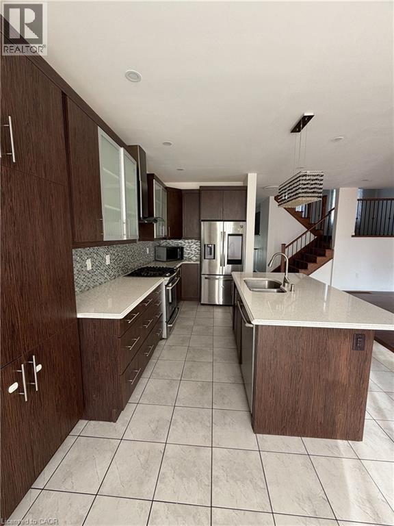 Modern kitchen featuring abundant dark wood-finish cabinetry, light-toned countertops, a mosaic tile backsplash, stainless steel appliances, and tile flooring - 235 Apple Hill Crescent, Kitchener, ON