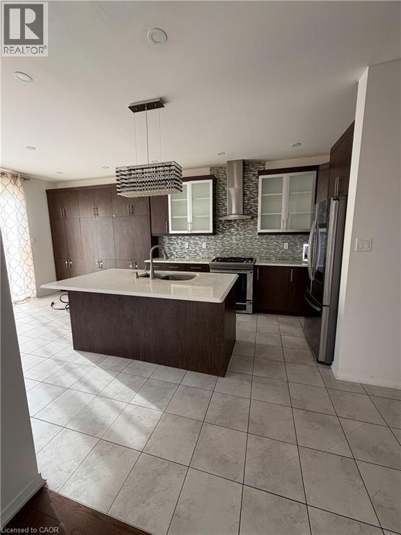Spacious kitchen featuring an expansive center island with an integrated sink, light-toned countertop, and dark wood-finish cabinetry - 235 Apple Hill Crescent, Kitchener, ON