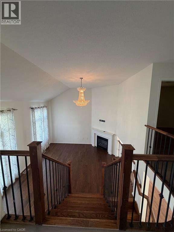 Open-concept living area with vaulted ceilings, a prominent chandelier, wood-finish flooring, and a fireplace with a white mantel - 235 Apple Hill Crescent, Kitchener, ON