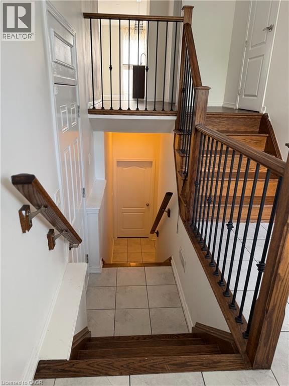 Hardwood staircase with wrought iron balusters leading to a tiled landing - 235 Apple Hill Crescent, Kitchener, ON