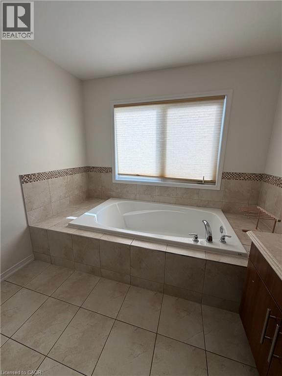 Built-in soaking tub with deck-mounted fixtures, surrounded by neutral-toned tile - 235 Apple Hill Crescent, Kitchener, ON
