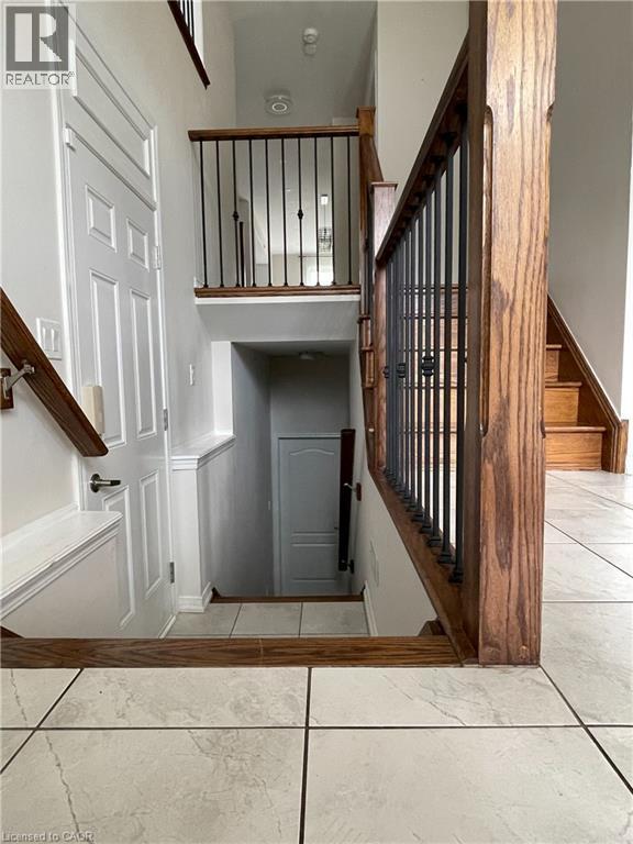 Multi-level interior featuring a wood-finish staircase with wrought iron balusters, light-toned tile flooring, and white paneled doors - 235 Apple Hill Crescent, Kitchener, ON