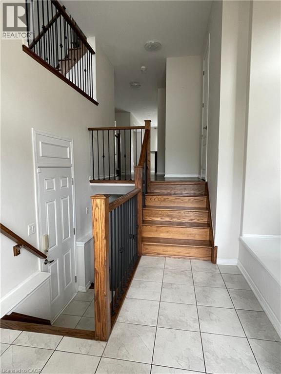 Multi-level interior featuring a wood staircase with wrought iron balusters, a tiled floor, white walls, and built-in shelving - 235 Apple Hill Crescent, Kitchener, ON
