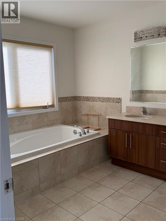 Soaking tub with tiled surround, accompanied by a wood-finish vanity with an integrated sink and a neutral stone-finish countertop - 235 Apple Hill Crescent, Kitchener, ON