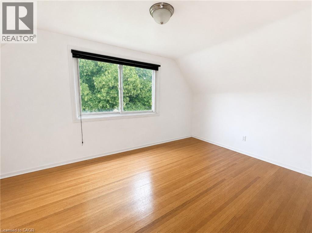 Light-filled room featuring wood-finish flooring, white baseboards, and a window with a black roller shade - 83 East 41St Street, Hamilton, ON - Indoor Photo Showing Other Room