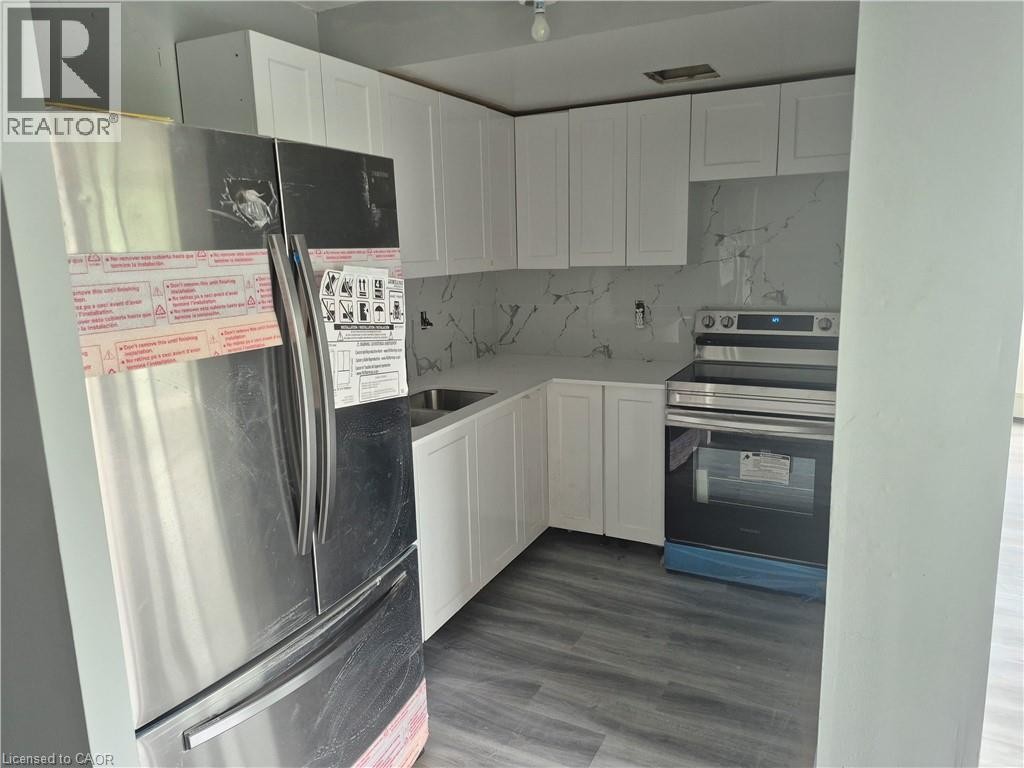Kitchen featuring white shaker cabinetry, stainless steel appliances, a white marble-look backsplash, white countertops, and wood-finish flooring - 150 Charlton Avenue E Unit# 708, Hamilton, ON