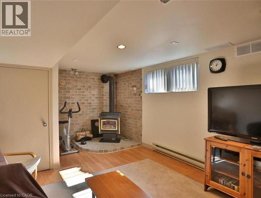 Finished basement area featuring wood-finish flooring, a brick accent wall, and a built-in wood-burning stove with a stone hearth - 92 Pattandon Avenue Unit# C, Kitchener, ON - Indoor Photo Showing Living Room With Fireplace