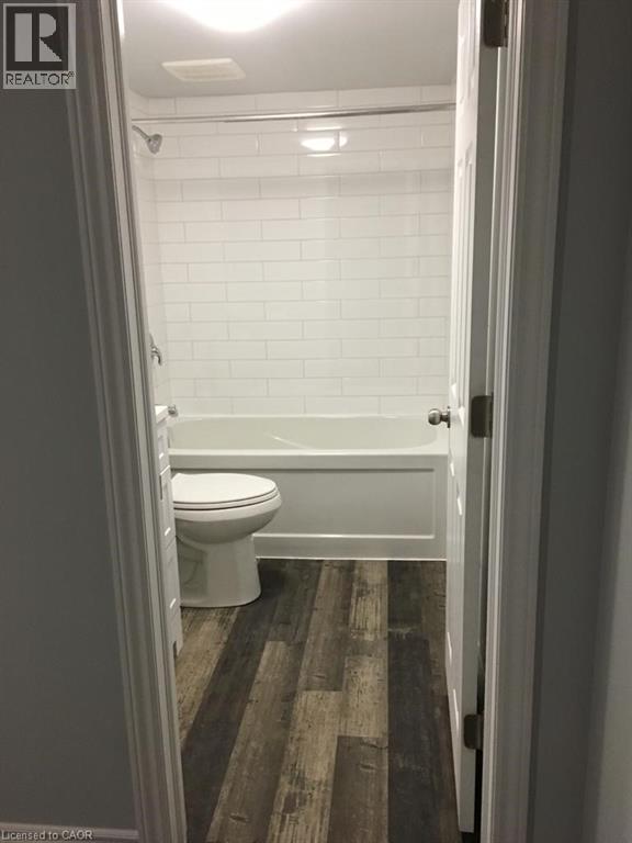 Bathroom featuring a white subway tile shower surround, a white bathtub, and wood-finish flooring - 92 Pattandon Avenue Unit# C, Kitchener, ON - Indoor Photo Showing Bathroom