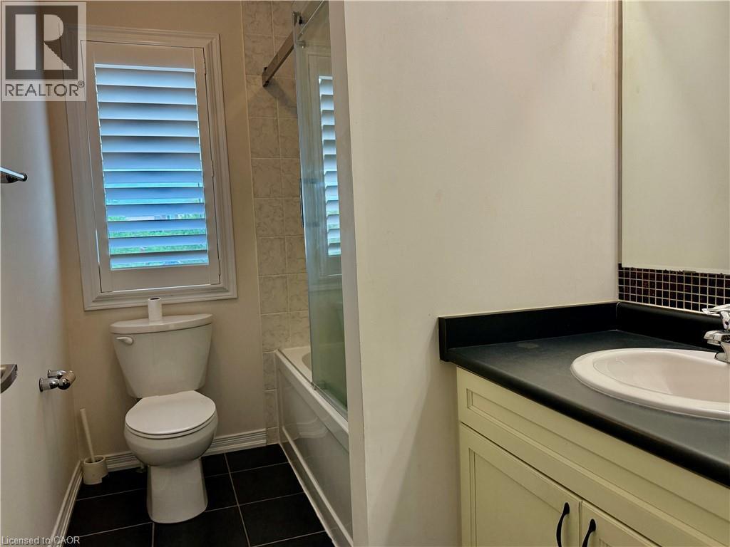Bathroom featuring dark tile flooring, a white toilet with a window above, and a white vanity with a dark countertop and integrated sink - 386 Apple Hill Crescent, Kitchener, ON
