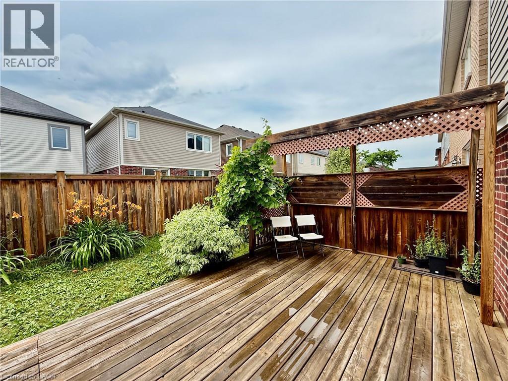 Expansive wood-finish deck with an integrated pergola featuring lattice accents, complemented by a privacy fence and garden beds with established plantings - 386 Apple Hill Crescent, Kitchener, ON