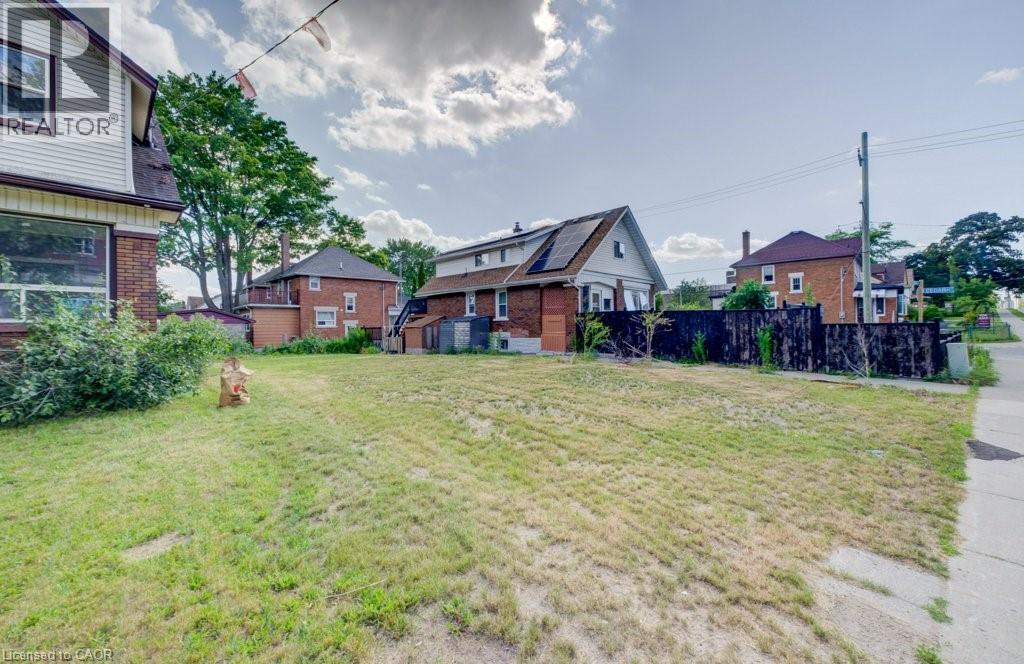 Expansive cleared lot with mature trees in the background, featuring a partial sidewalk and existing perimeter fencing - 153 Courtland Avenue E, Kitchener, ON