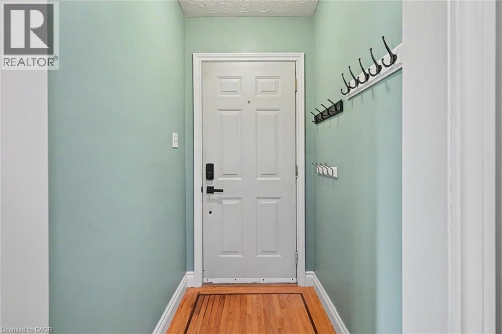 Entryway featuring a paneled door with modern hardware, wood-finish flooring, light green wall finishes, and white trim - 56 Everton Place, Hamilton, ON