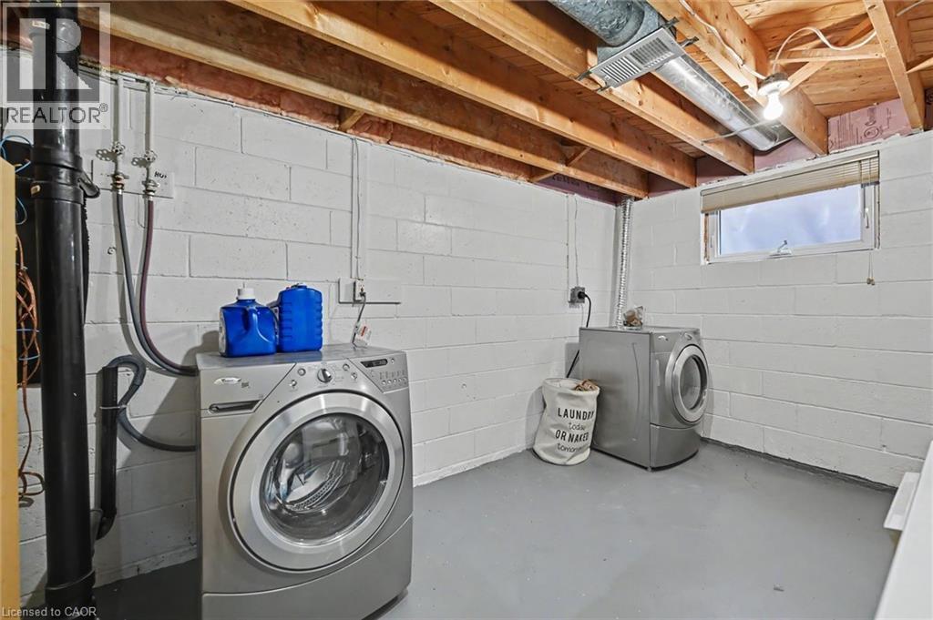 Laundry area featuring white painted cinder block walls, exposed wood ceiling joists, and a painted concrete floor - 56 Everton Place, Hamilton, ON