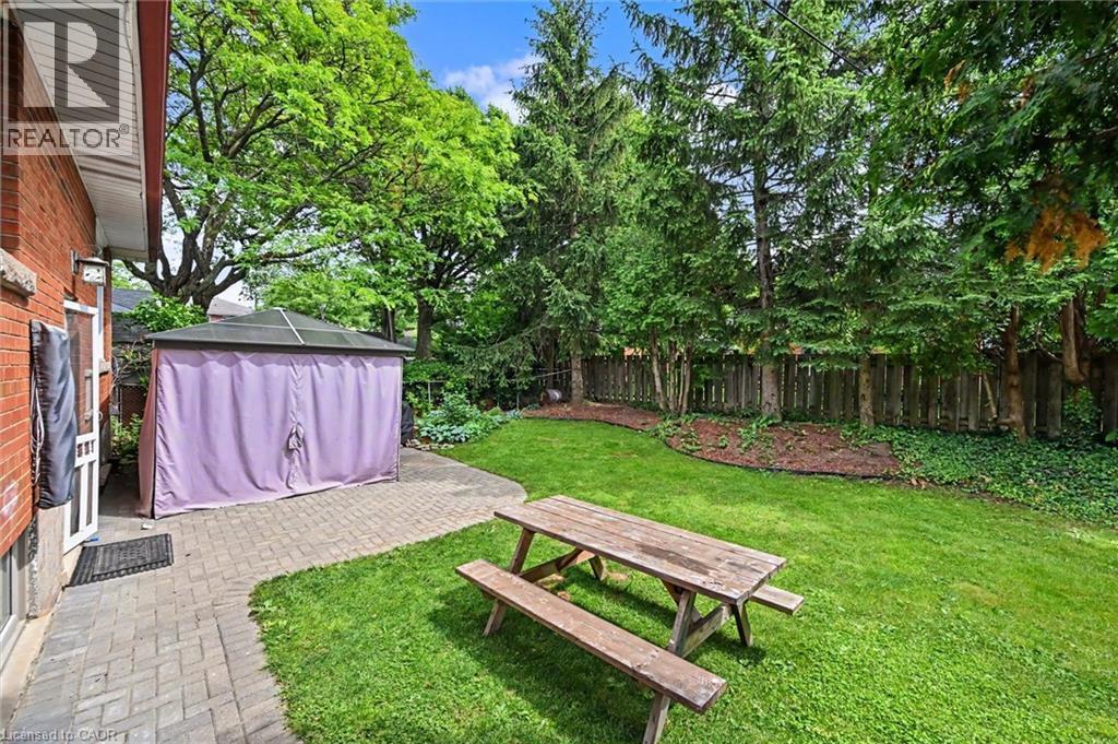 Expansive green lawn with mature perimeter trees, a paver patio, and a privacy fence - 56 Everton Place, Hamilton, ON