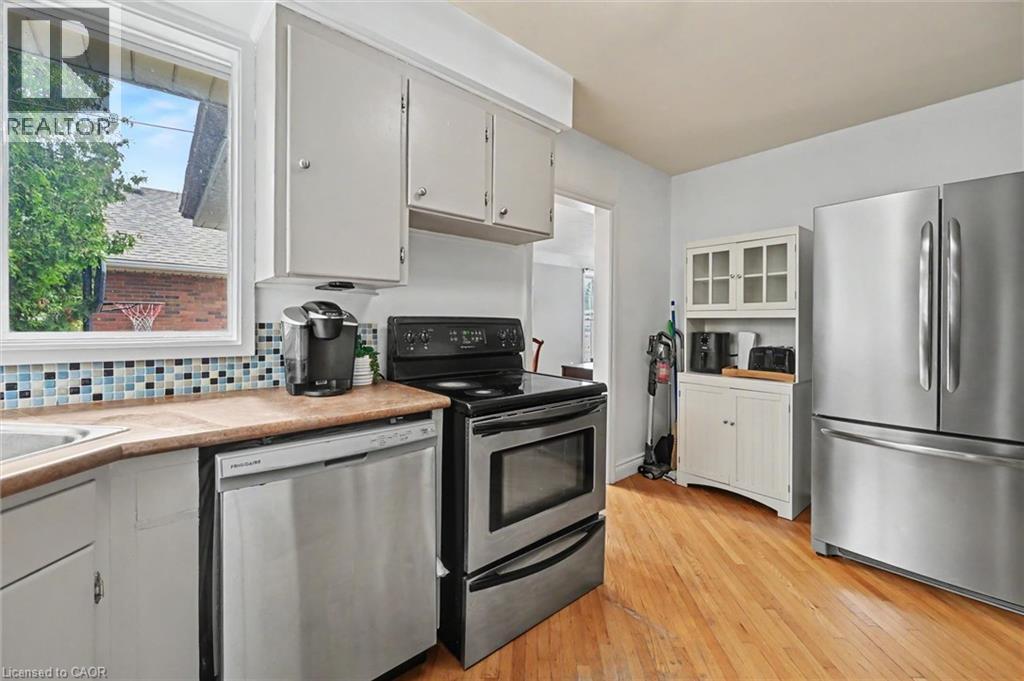 Kitchen featuring stainless steel appliances, light wood-finish flooring, white cabinetry, a mosaic tile backsplash, and a window above the sink - 56 Everton Place, Hamilton, ON