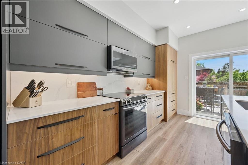 Modern kitchen featuring two-tone cabinetry, stainless steel appliances, white countertops, and wood-finish flooring - 63 Plymouth Road, Kitchener, ON