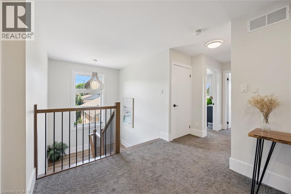 Carpeted hallway with a wood-finish and black metal spindle railing overlooking a staircase - 63 Plymouth Road, Kitchener, ON