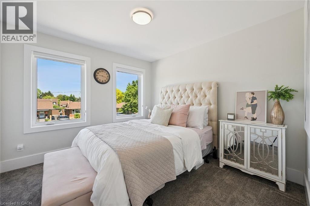 Light-filled room featuring wall-to-wall carpeting, two large windows with white trim, a flush-mount ceiling light, and neutral wall paint - 63 Plymouth Road, Kitchener, ON