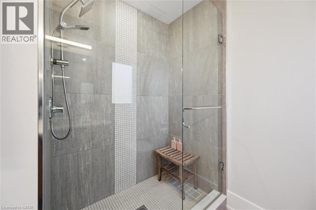 Glass-enclosed shower featuring large format wall tiles, a mosaic tile accent stripe, and a dual shower head system - 63 Plymouth Road, Kitchener, ON