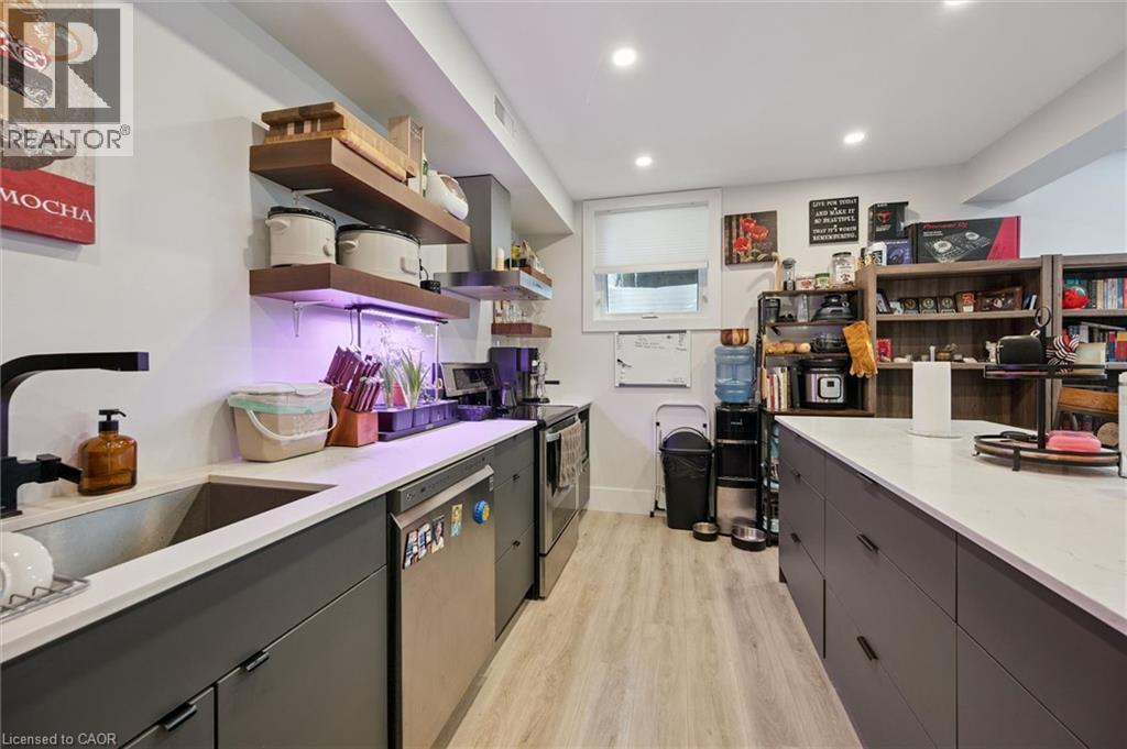 Modern kitchen featuring dark cabinetry, stainless steel appliances, and light wood-finish flooring - 63 Plymouth Road, Kitchener, ON