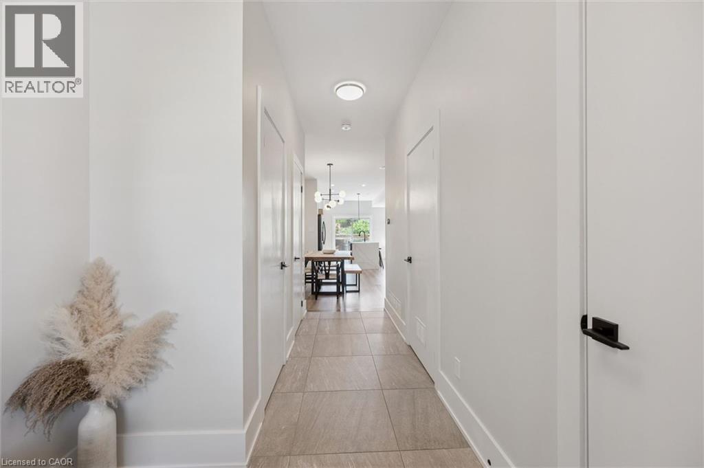Hallway featuring light-toned tile flooring, white walls, and contemporary black door hardware - 63 Plymouth Road, Kitchener, ON