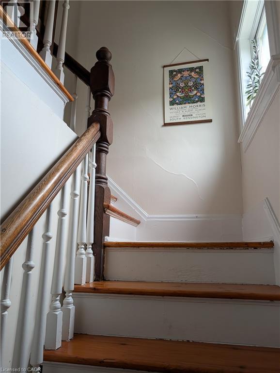 Staircase featuring wood-finish treads and handrail, white painted risers and balusters, and a substantial newel post - 15 Martin Street, Kitchener, ON