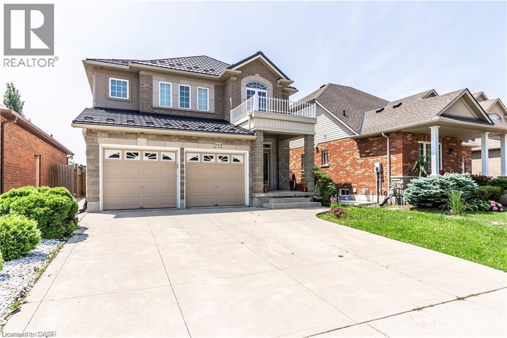 Two-story residence featuring a combination of brick and stone facade, a two-car garage with arched window inserts, and a prominent front entrance with a second-story balcony - 252 Thorner Drive Unit# Basement, Hamilton, ON