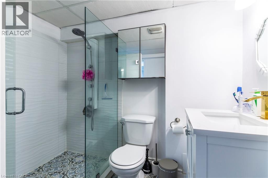 Bathroom featuring a glass-enclosed shower with patterned floor tiles, wave-textured shower wall tiles, a white vanity with an integrated sink, a gold-finish faucet, and a wall-mounted medicine cabine - 252 Thorner Drive Unit# Basement, Hamilton, ON