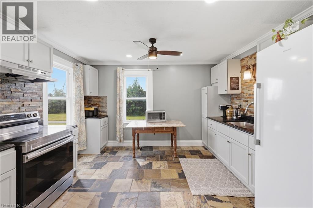 Spacious kitchen featuring white cabinetry, stone-look tile flooring, and a stone accent wall - 97 Smith Road, Hamilton, ON