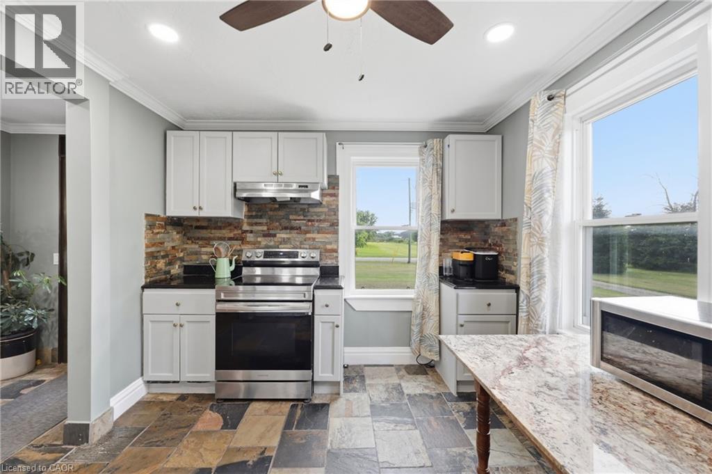 Kitchen featuring light gray cabinetry, dark countertops, a stacked stone backsplash, stainless steel appliances, and multi-toned slate flooring - 97 Smith Road, Hamilton, ON
