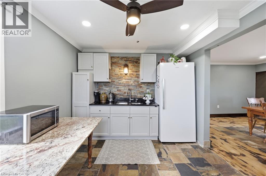 Kitchenette featuring white cabinetry, a dark countertop, a stone-finish backsplash, and multi-tone tile flooring - 97 Smith Road, Hamilton, ON