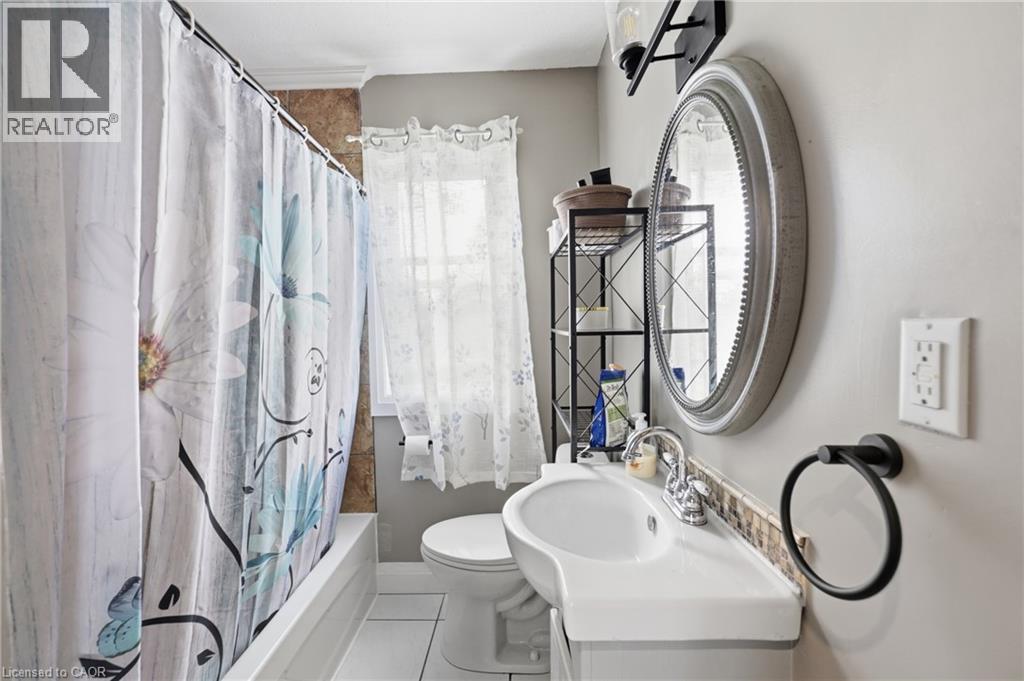 Bathroom featuring a single vanity with an integrated sink, a circular framed mirror, and a tub with a shower - 97 Smith Road, Hamilton, ON