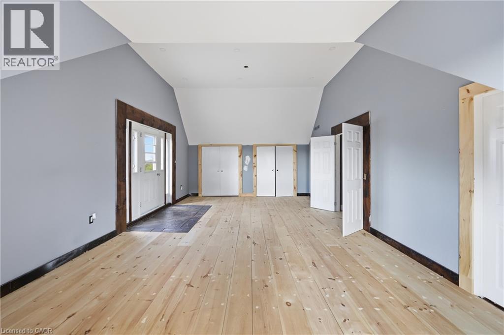 Expansive attic space featuring light wood-finish flooring, vaulted ceilings, light blue walls, and multiple panel doors - 97 Smith Road, Hamilton, ON
