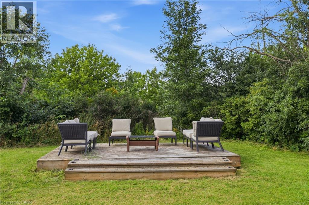 Outdoor wooden deck with integrated steps, surrounded by green lawn and mature trees - 97 Smith Road, Hamilton, ON