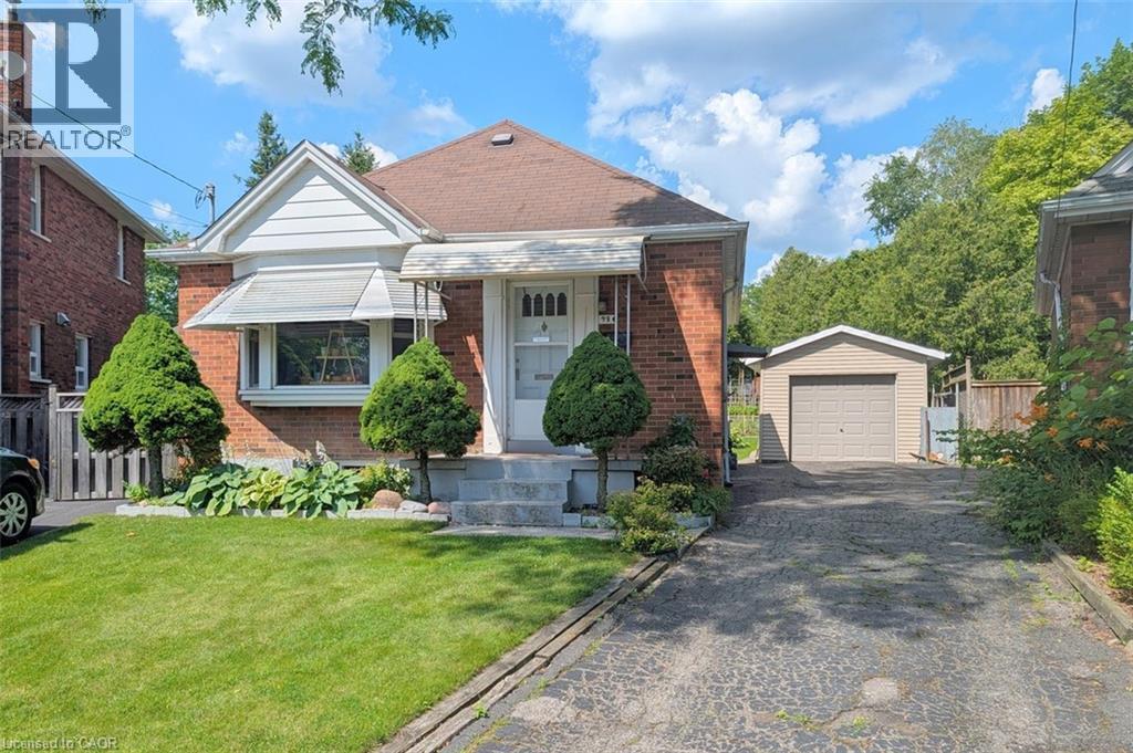 Brick exterior featuring a front lawn, bay window with awning, concrete front steps, a paved driveway, and a detached garage - 98 Kipling Road Unit# 2, Hamilton, ON