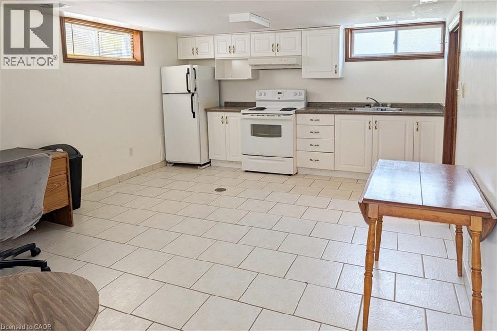Bright kitchen space featuring white cabinetry, a white electric range, white refrigerator, a double basin sink, and tile flooring - 98 Kipling Road Unit# 2, Hamilton, ON