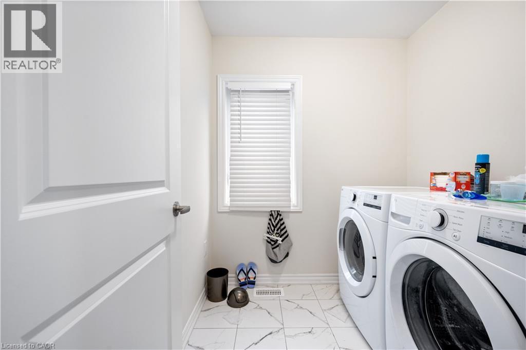 Laundry area featuring a front-loading washer and dryer set, a single window with blinds, and white panel doors - 61 Vanilla Trail, Thorold, ON
