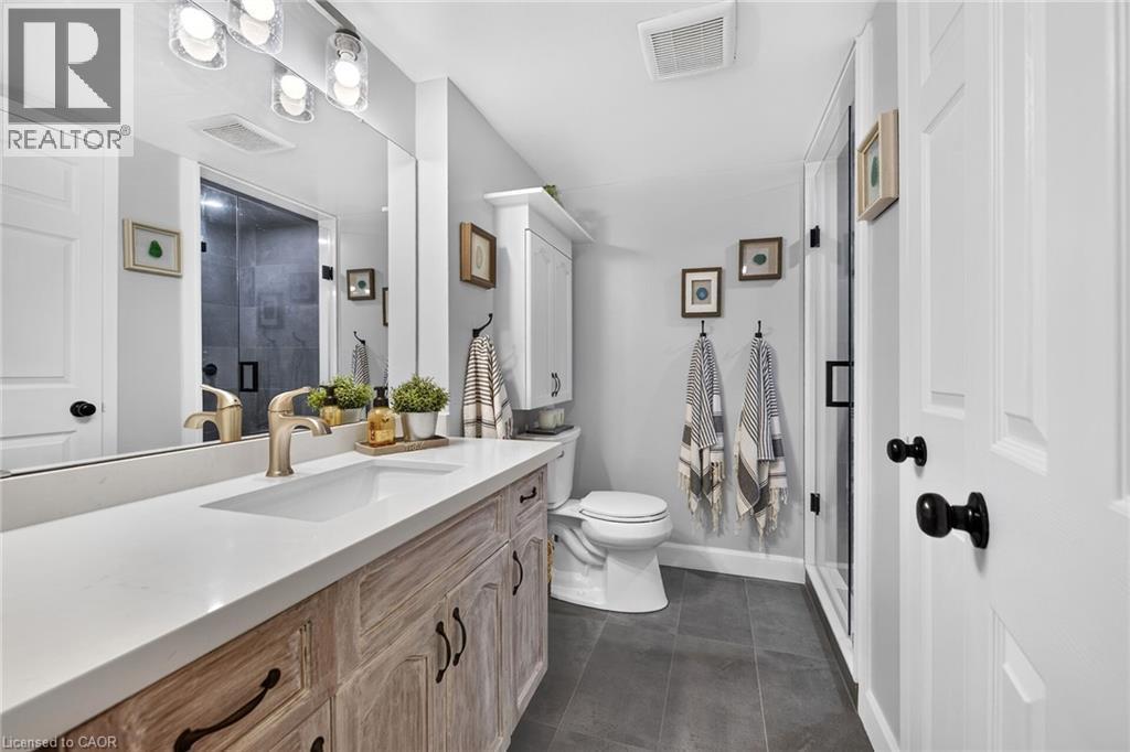 Bathroom featuring a vanity with a light wood-finish cabinet and white countertop, integrated sink with a gold-tone faucet, and an overhead vanity light fixture - 1237 North Shore Boulevard Unit# 405, Burlington, ON - Indoor Photo Showing Bathroom