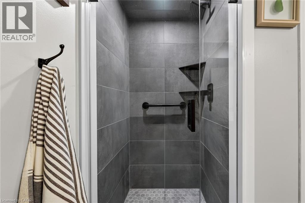 Enclosed shower featuring full-height gray tile, a hexagonal mosaic floor, and matte black fixtures - 1237 North Shore Boulevard Unit# 405, Burlington, ON - Indoor Photo Showing Bathroom