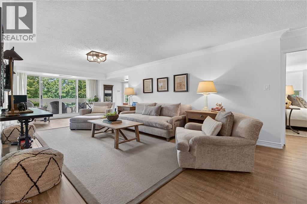 Spacious living area featuring wood-finish flooring, white walls, and crown molding - 1237 North Shore Boulevard Unit# 405, Burlington, ON - Indoor Photo Showing Living Room