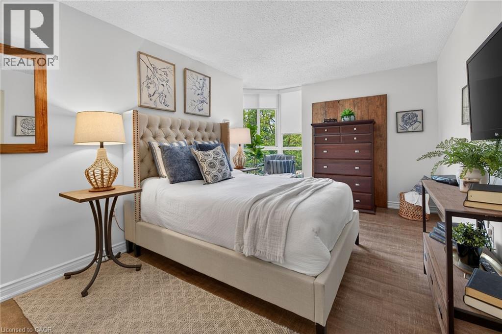 Bright sleeping area featuring wood-finish flooring, white walls, and a large bay window - 1237 North Shore Boulevard Unit# 405, Burlington, ON - Indoor Photo Showing Bedroom