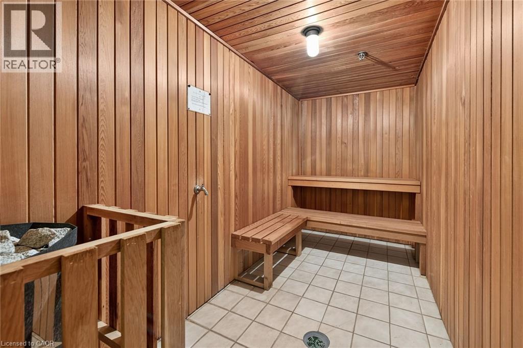 Wood-paneled sauna featuring tiered wooden benches, a built-in heater with protective railing, and square tile flooring - 1237 North Shore Boulevard Unit# 405, Burlington, ON - Indoor Photo Showing Other Room