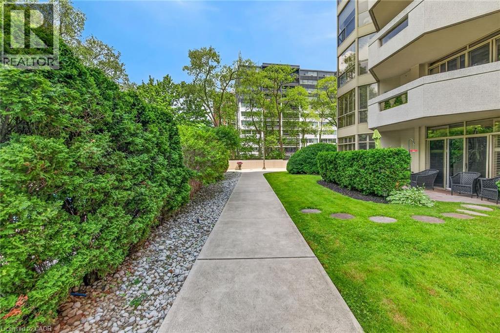 Concrete pathway bordered by manicured hedges and a gravel bed - 1237 North Shore Boulevard Unit# 405, Burlington, ON - Outdoor With Balcony