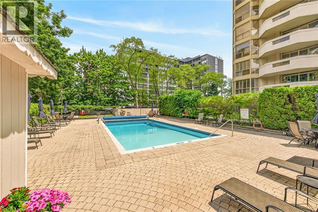 Outdoor swimming pool surrounded by a large paver patio, lush perimeter landscaping, and mature trees - 1237 North Shore Boulevard Unit# 405, Burlington, ON - Outdoor With In Ground Pool