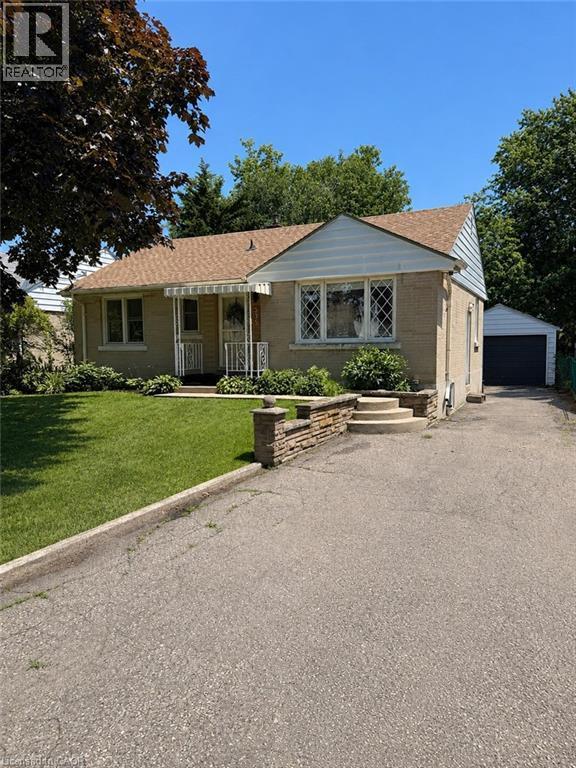Brick exterior with a peaked roofline, front lawn, stone retaining wall, and an attached garage - 355 East 36Th Street, Hamilton, ON