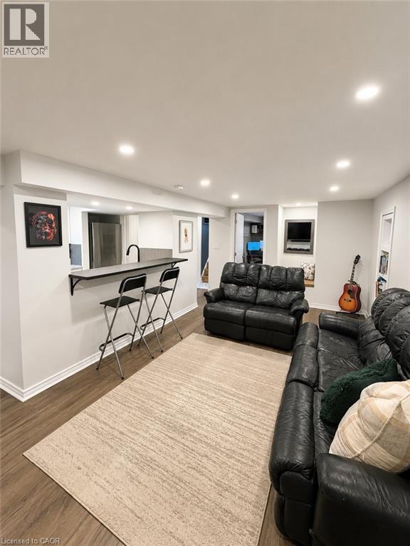 Open-concept living space featuring recessed lighting, wood-finish flooring, a built-in wet bar with a dark countertop and black faucet, and white baseboards - 355 East 36Th Street, Hamilton, ON