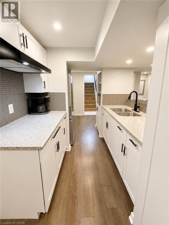 Galley kitchen featuring white cabinetry with black hardware, light-toned countertops, a stainless steel sink with a black faucet, and wood-finish flooring - 355 East 36Th Street, Hamilton, ON